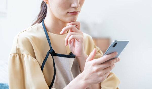 スマホ画面を怪訝な表情で眺める女性のイメージ画像