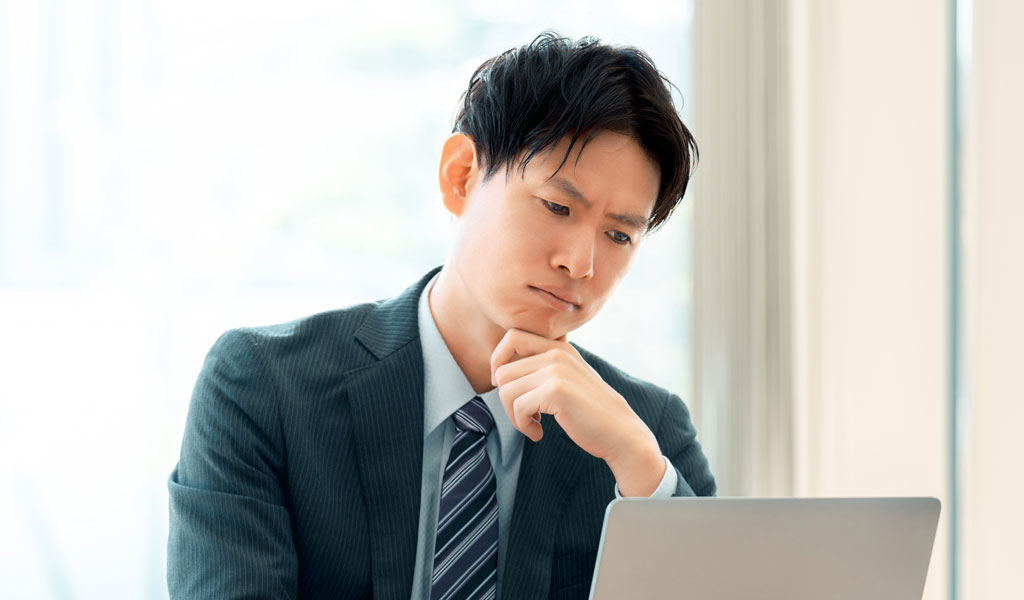 パソコンの画面を眺め、訝しむ表情の男性のイメージ画像